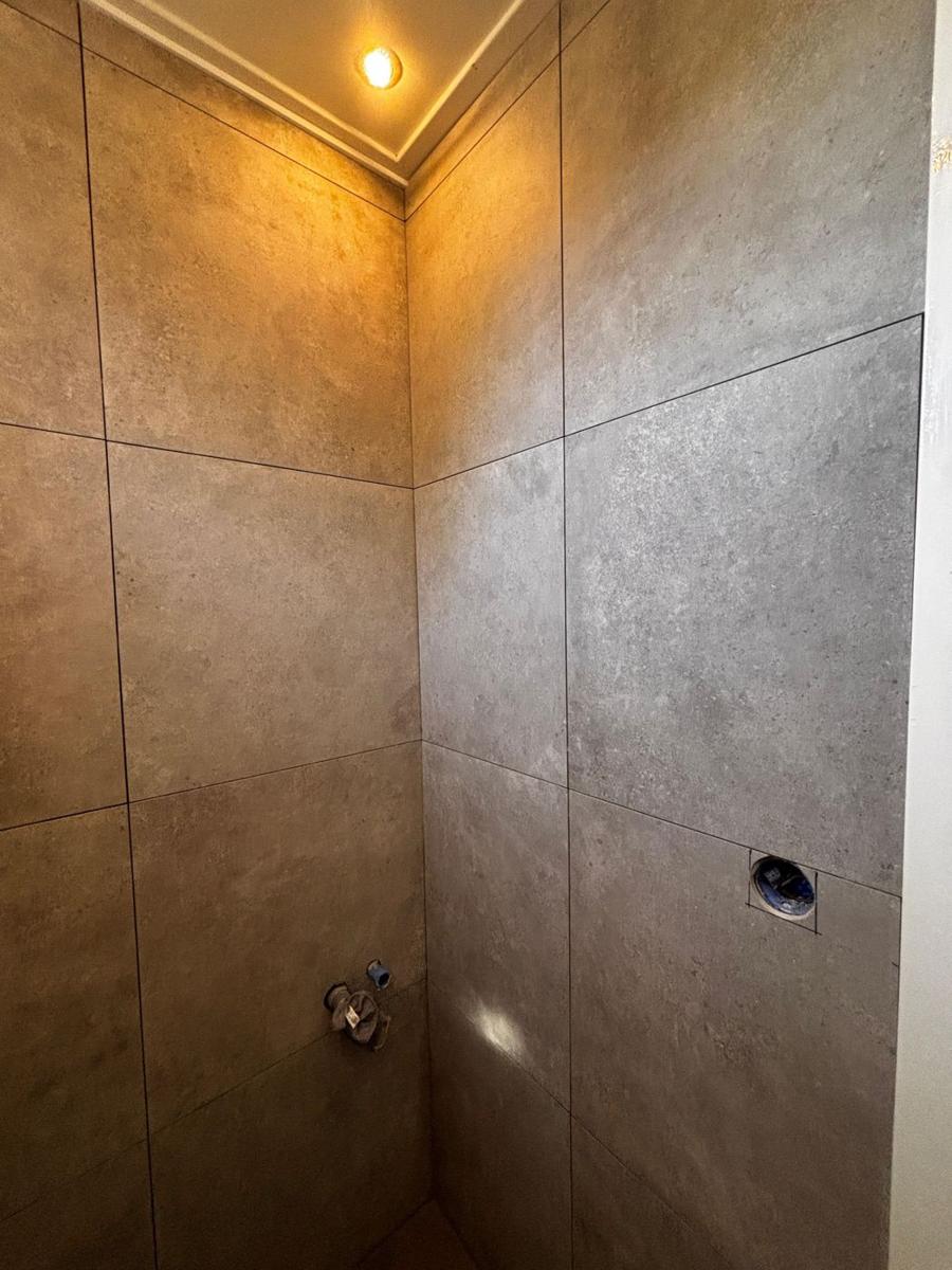 Douchehoek met grote beige natuursteenlook tegels en inbouwspot